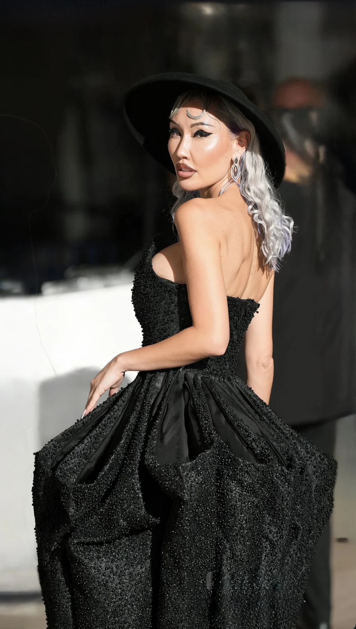 Silver waves beneath a black hat, with a sculptural black gown